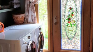Ein Waschraum mit einer Waschmaschine, einem Wäscheständer und einem Fenster mit einer Glasbibrandtür.