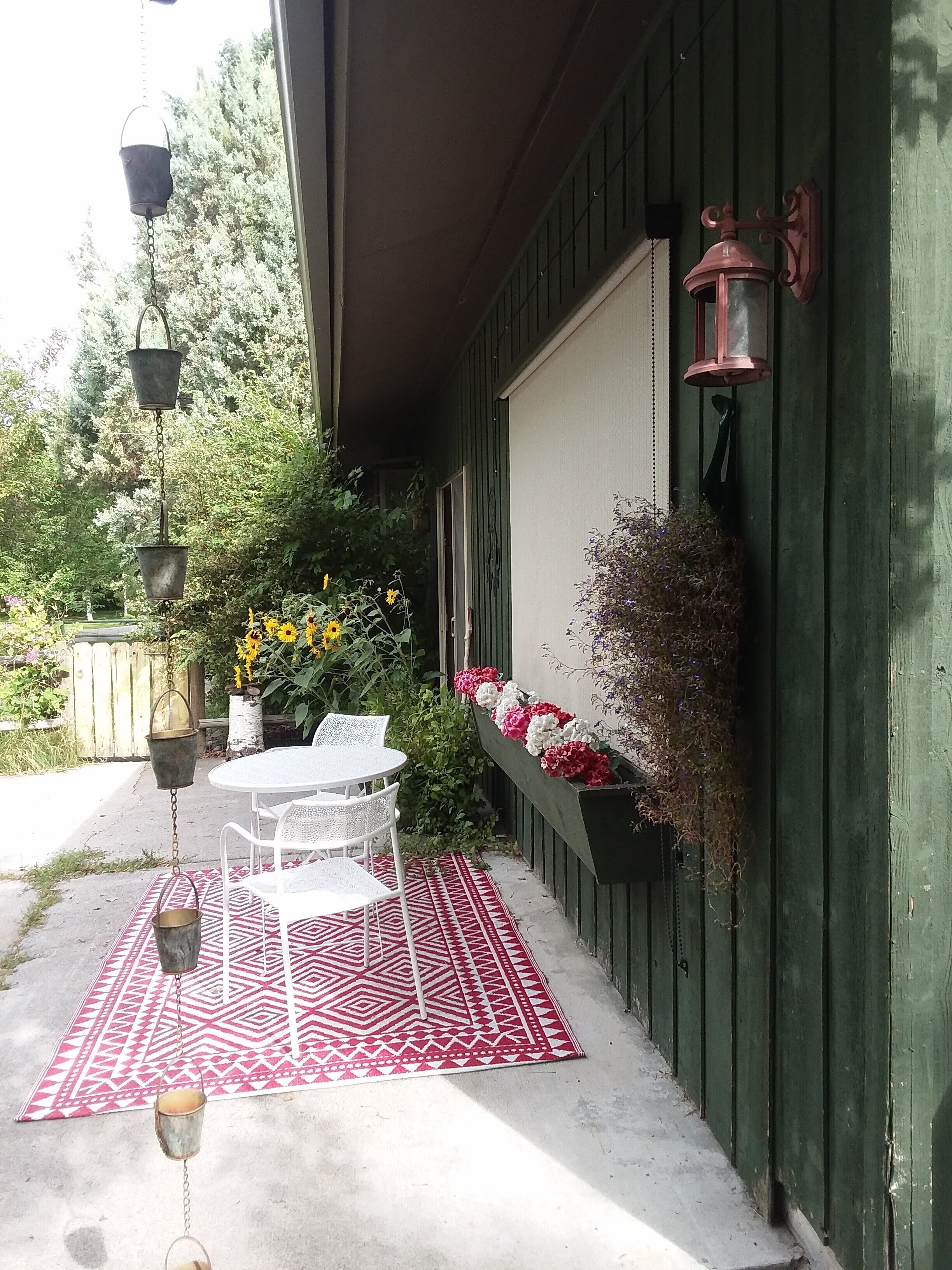 A patio with a table and chairs, hanging planters, and a red patterned rug.