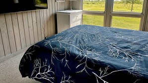 Quarto com cama, televisão, espelho, cômoda e janela com vista para o verde.