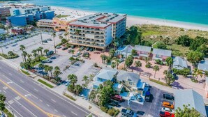 An aerial view of a coastal hotel with a parking lot, beach access, and a clear view of the ocean. - Suncoast Getaway – Walk to Sand & Shops (Madeira Beach)