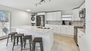 A modern kitchen with a large island, bar stools, a washing machine, a refrigerator, and a microwave. - Suncoast Getaway – Walk to Sand & Shops (Madeira Beach)