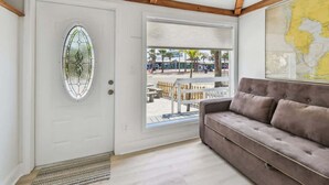 A room with a white door, a large window, a grey sofa, and a map on the wall. - Suncoast Getaway – Walk to Sand & Shops (Madeira Beach)