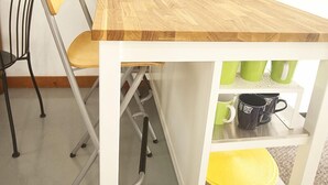 Una piccola cucina con un piano di lavoro in legno, una macchina da caffè e un bollitore. C'è una sedia e uno scaffale con tazze.