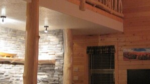 Interior de madera con balcón, chimenea de piedra y ventilador de techo.
