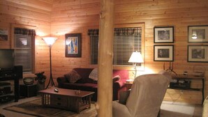 Acogedor interior de cabaña de madera con sofá, sillón y televisor.