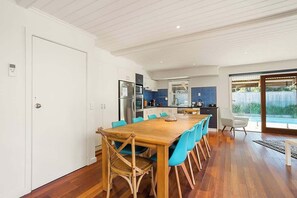 A modern kitchen with built-in appliances, a dining area with a wooden table and blue chairs, and a sliding glass door leading to an outdoor area.