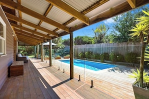 A covered outdoor area with a pool, wooden deck, and seating.