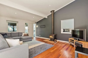 A modern living room with a sofa, a television, a fireplace, and a large window.
