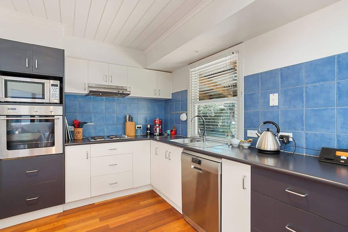 Una cocina moderna con electrodomésticos de acero inoxidable, armarios blancos y azulejos azules.