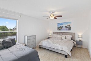 A bedroom with a bed, a dresser, and a nightstand. There is a window with a view of a body of water and greenery.