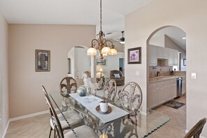 A dining area with a glass table, ornate chairs, and a chandelier.