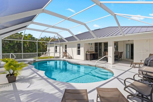 A covered outdoor swimming pool with lounge chairs and a barbecue area.