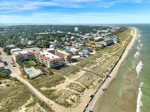 Vue aérienne d’une ville côtière avec des propriétés situées en bord de mer, un phare et une promenade en bord de plage.