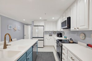 A modern kitchen with white cabinets, a stainless steel sink, a built-in oven, and a microwave.