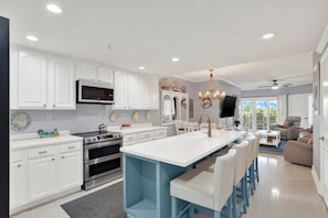 A modern kitchen with white cabinetry, a central island, and a dining area with a view. - Ocean View Condo on Tybee Island | Pool Access (Tybee Island)
