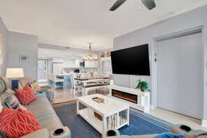 A modern living room with a sofa, coffee table, flat-screen TV, fireplace, and a kitchen in the background.