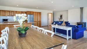 A modern kitchen with wooden cabinets, a dining table with chairs, a blue sofa, and a fireplace. - Uninterrupted Views Encounter Bay (Encounter Bay)