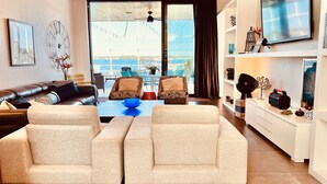 Una sala de estar moderna con un sofá de cuero, sillones color beige, una mesa de centro y vistas al mar a través de amplios ventanales.