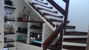 A staircase with a wooden handrail and white steps, leading to a landing with a TV displaying news. - Juquehy, beachfront, almost on the sand, special offer February/26, 6 people. (São Sebastião)