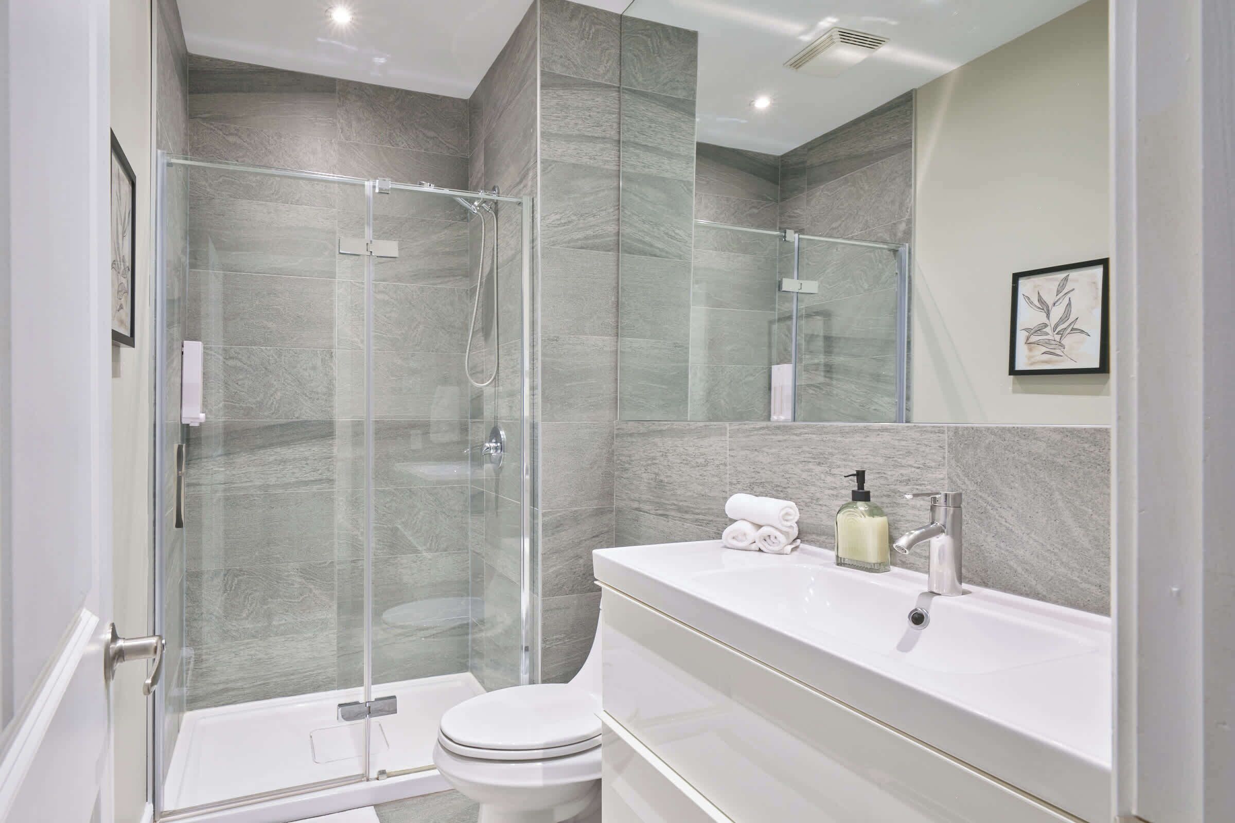 Un baño moderno con ducha de vidrio, inodoro blanco y tocador con espejo y lavabo.