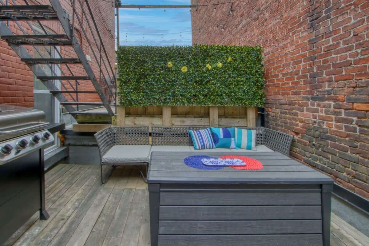 En terrasse med et træbord, grill og en siddeplads med puder.