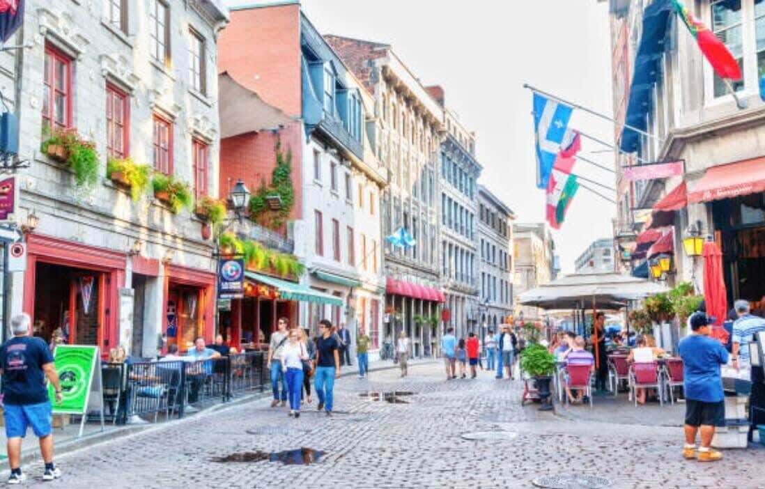 En kullerstensgata kantad av historiska byggnader, uteserveringar för caféer och flaggor.