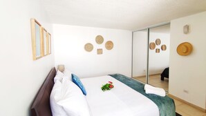 A neatly made bed with white and blue bedding, a small plant, and a mirror reflecting the room. - Beach Front & 3 levels & Terrace & Balcony & 2 Pools Max 6people (Río Grande)