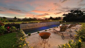 A poolside area with a barbecue, lounge chairs, and a view of a golf course at sunset.