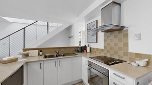 A modern kitchen with white cabinets, a stainless steel range hood, and a skylight above the staircase. - Noosa Sound, waterfront, amazing value (NOOSA HEADS)
