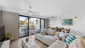 A modern living room with a sofa, coffee table, and a dining area with chairs and a table. - Noosa Sound, waterfront, amazing value (NOOSA HEADS)