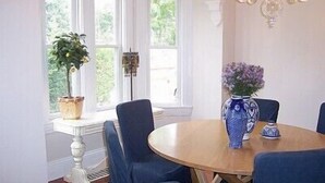 A dining area with a round table, blue chairs, a vase with flowers, and a chandelier.
