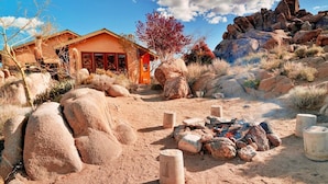 A desert-style house with a fire pit and large rocks in the foreground. - The Joshua Tree Oasis, Joshua Tree Oasis Home (Joshua Tree)