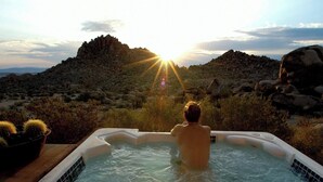 A person in a hot tub with a mountainous landscape in the background. - The Joshua Tree Oasis, Joshua Tree Oasis Home (Joshua Tree)