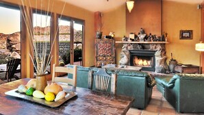 A cozy living room with a fireplace, comfortable seating, and a dining area with a tray of bread and eggs. - The Joshua Tree Oasis, Joshua Tree Oasis Home (Joshua Tree)