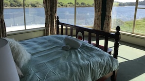 A bedroom with a large window offering a view of a lake and hills.