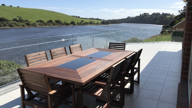 A wooden table and chairs on a terrace with a view of a river and green hills.