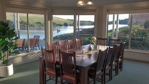 A dining area with a large table and chairs, large windows with a view of a lake and hills.