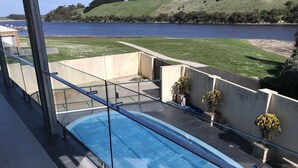 A swimming pool with a glass railing, a view of a lake, and a grassy area with trees.