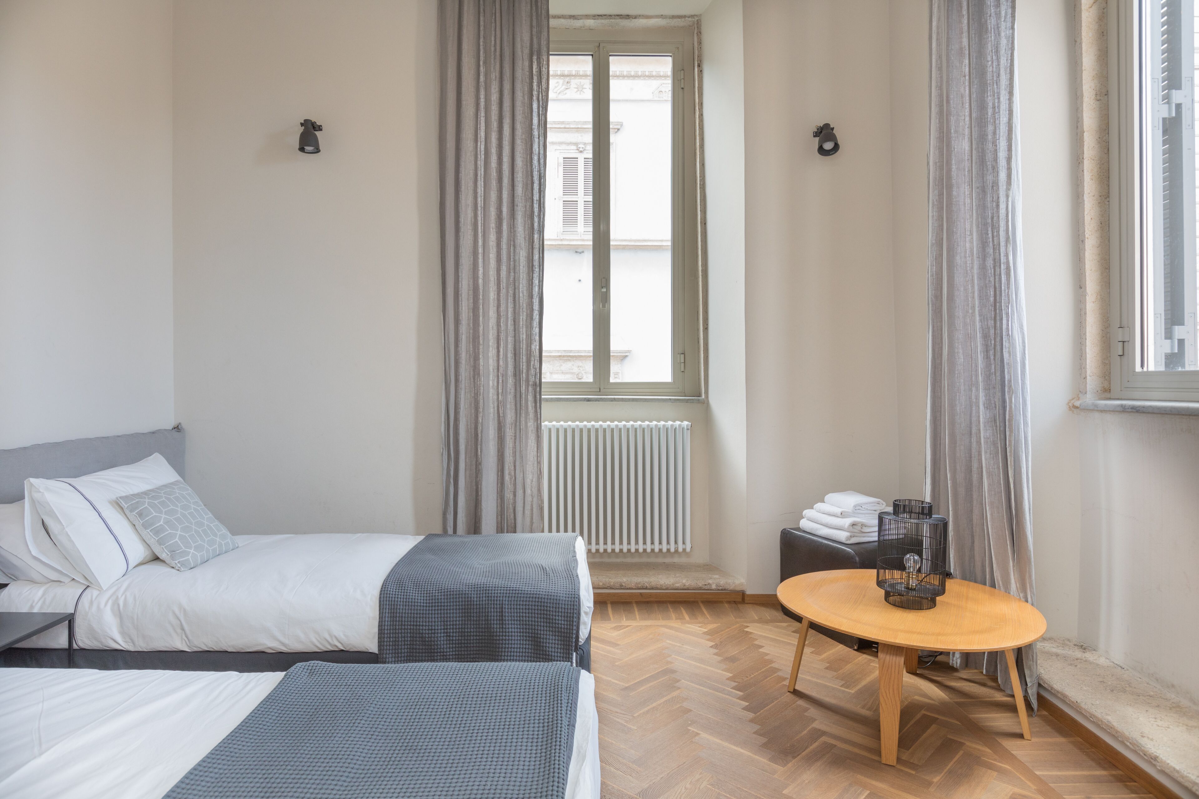 Une chambre d’hôtel avec deux lits, un plancher en bois, une table ronde avec une bougie et une fenêtre avec des rideaux.