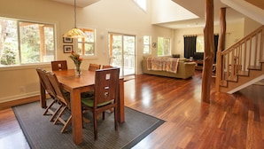 Un salón espacioso con una mesa de comedor de madera, sillas y un sofá. Se ve una escalera con barandillas de madera que sube a un nivel superior.