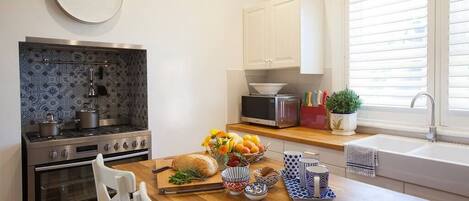 A modern kitchen with a stove, oven, microwave, and a window with blinds.