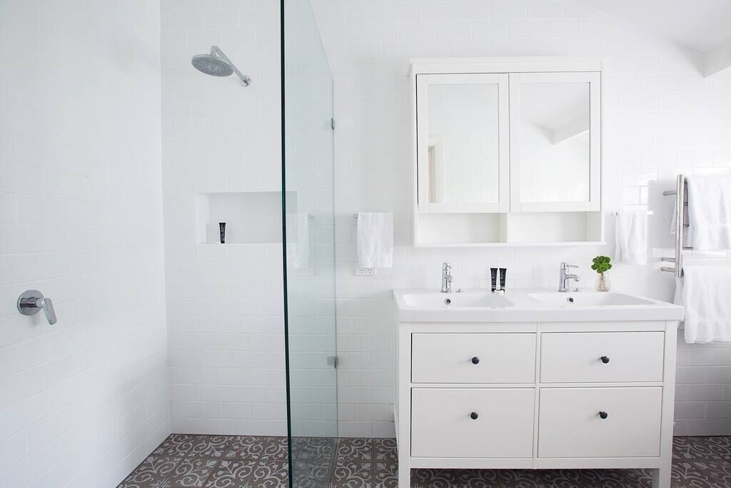 Un baño moderno con cabina de ducha de vidrio, tocador blanco con espejo y baldosas de suelo estampadas.