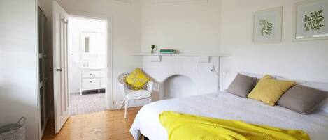 A bedroom with a bed, a fireplace, a chair, and a shelf with books.