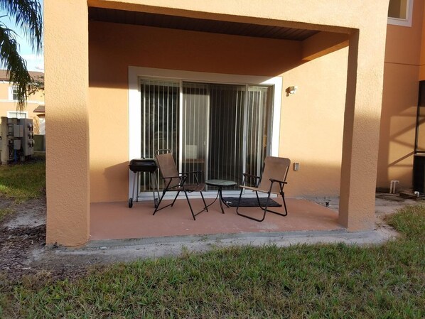 An outdoor patio with a table and two chairs, a sliding glass door, and a concrete floor. - 4 BR unit with 2 King Size Ensuite BR , 3 Mi to Disney, 1 min to Pool, Free WiFi (Kissimmee)