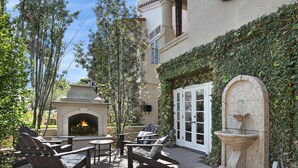 An outdoor patio with a stone fireplace, lounge chairs, and a stone fountain. - Luxury beach home with outside fireplace and dining, 10 minute walk to beach  (Newport Beach)