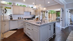 A spacious kitchen with white cabinetry, a large island, and a view of the backyard through an open door. - Luxury beach home with outside fireplace and dining, 10 minute walk to beach  (Newport Beach)