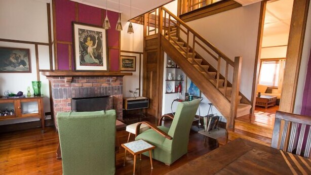 A cozy living room with a fireplace, green armchairs, a wooden staircase, and a bookshelf. - Beachside - Beauty Point. 
Unique Spacious Waterfront Pet-friendly (Beauty Point)