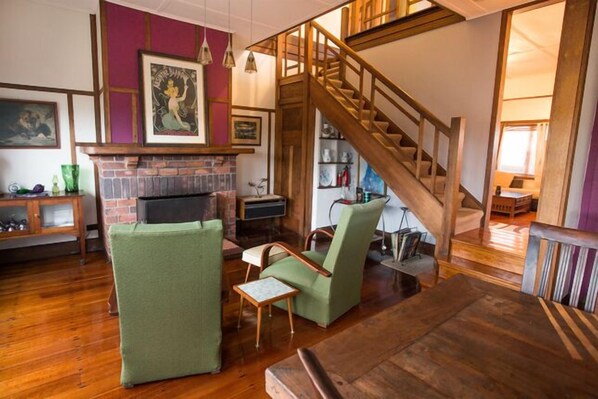 A cozy living room with a fireplace, green armchairs, a wooden staircase, and a bookshelf. - Beachside - Beauty Point. 
Unique Spacious Waterfront Pet-friendly (Beauty Point)
