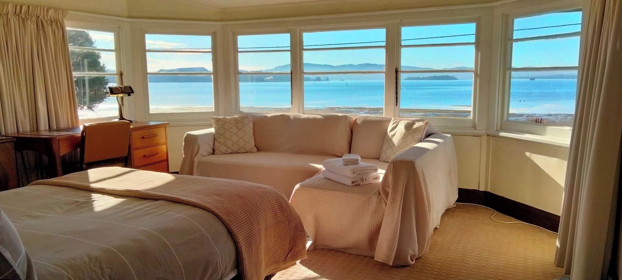 A hotel room with a bed, a sofa, a desk, and a view of the sea.