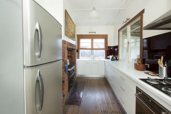 A kitchen with white cabinets, a stainless steel refrigerator, a brick fireplace, and a large window.